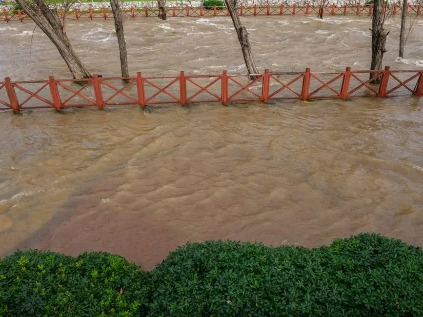 A city park flooded by a swollen river after heavy rainfall, showing the impact of severe weather.