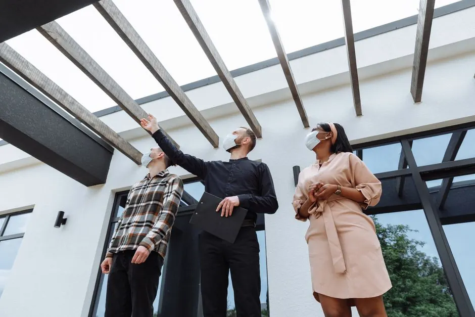 Masked real estate agent showcases modern architecture to clients outdoors.